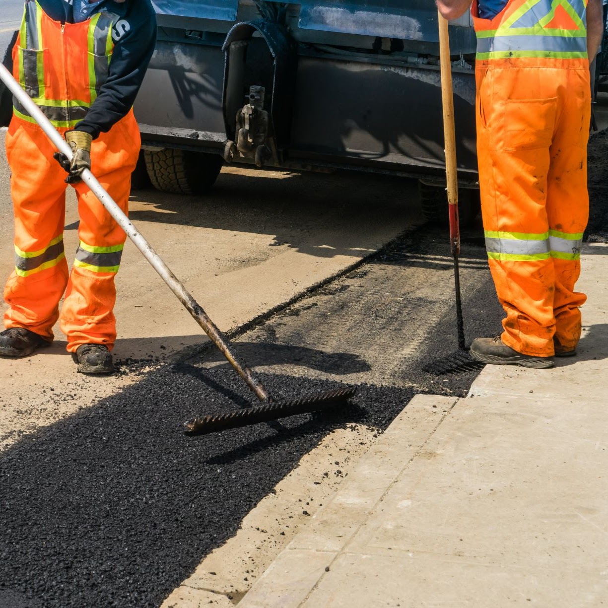 Two employees performing asphalt patch repairs with a brush-like tool, showcasing the expert services of Morris Town Paving, operating out of Morris County, NJ.