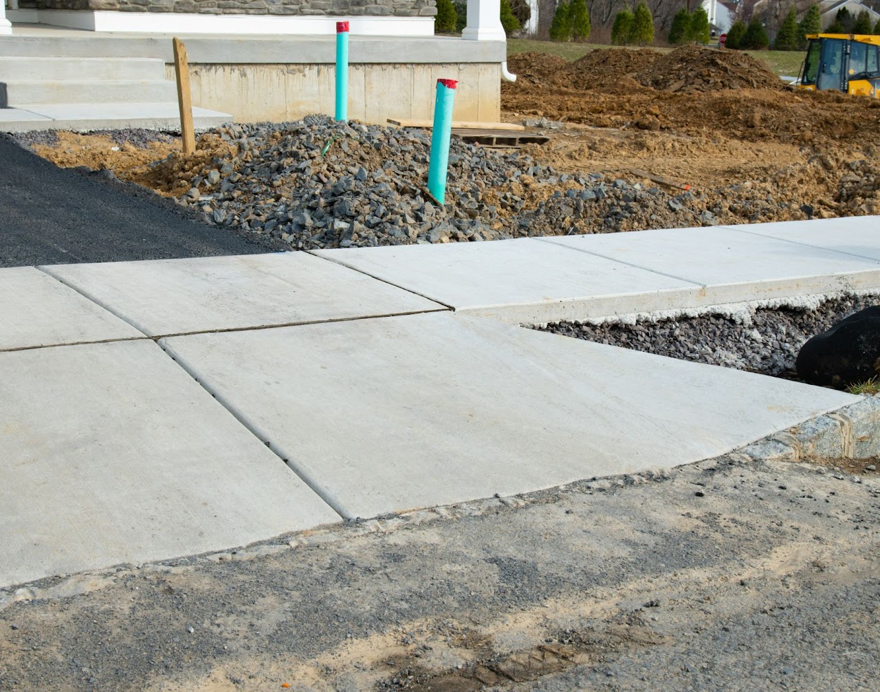 A freshly installed concrete sidewalk and curb under construction, with gravel and soil in the background, showcasing Morris Town Paving's sidewalk and curb installation and repair services in Morris County, NJ.