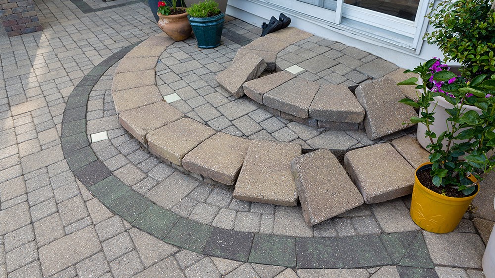 A curved entryway with custom beige pavers and charcoal border installed by Morristown Paving at a client's residence in Morris County, NJ. It features decorative curved steps lead to a glass door, with potted flowers adding color to the elegant design, showcasing our Decorative Paving services.