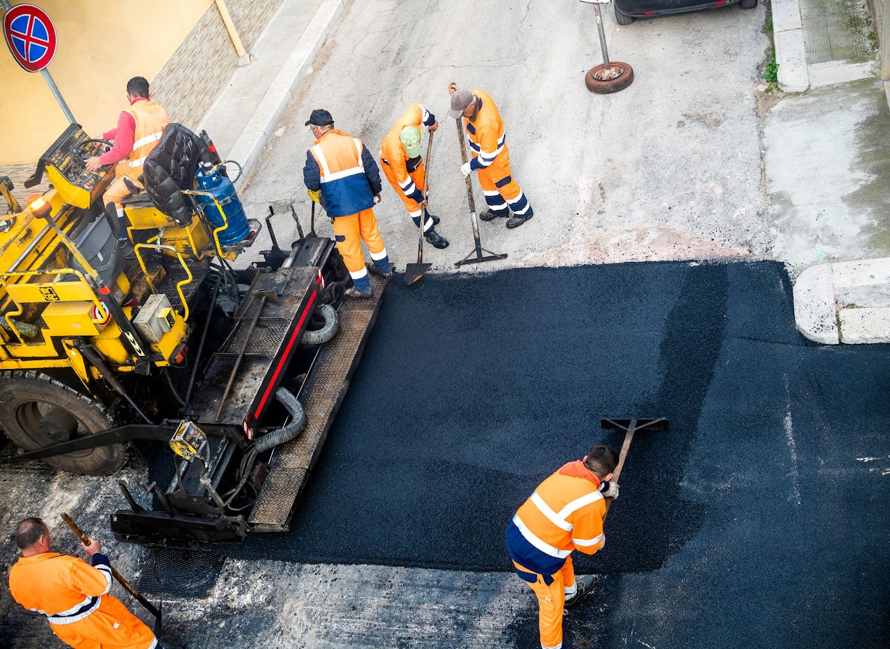 An aerial view of Morristown Paving crew members in Morris County, NJ working with fresh asphalt. Workers in high-visibility orange safety vests operate a paving machine laying down smooth black asphalt, demonstrating their professional road paving capabilities.