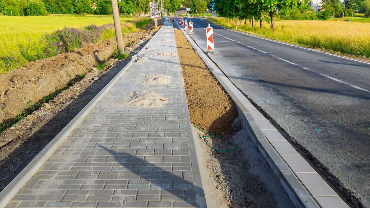 A newly constructed concrete sidewalk and curb with a decorative design and visible gravel and construction work, where Morristown Paving Professionals recently completed Sidewalk and Curb Installation and Repair services in Morris County, NJ.
