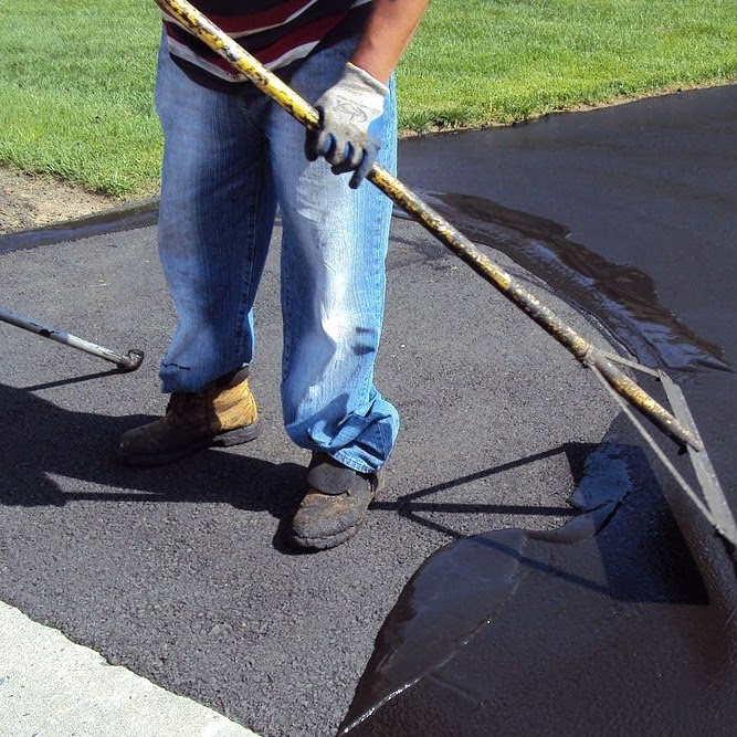 Worker from Morris Town Paving uses a hand-held smoothing tool to level and finish freshly laid asphalt on a residential driveway in Morris County, New Jersey. The professional crew member is focused on ensuring an even, smooth surface for the client's driveway renovation project