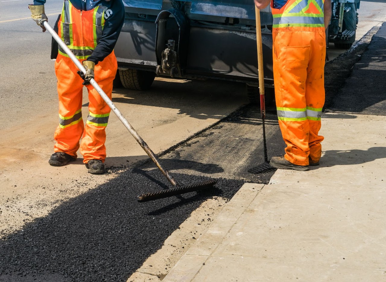Two workers applying asphalt to finish up patch repairs with specialized brush-like tools, highlighting the skill and professionalism of Morris Town Paving for client in Morris County, NJ.