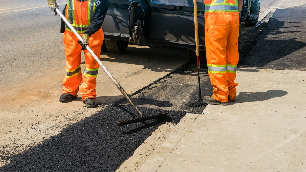 Two workers applying asphalt patch repairs with specialized brush-like tools, highlighting the skill and professionalism of Morris Town Paving, based in Morris County, NJ.