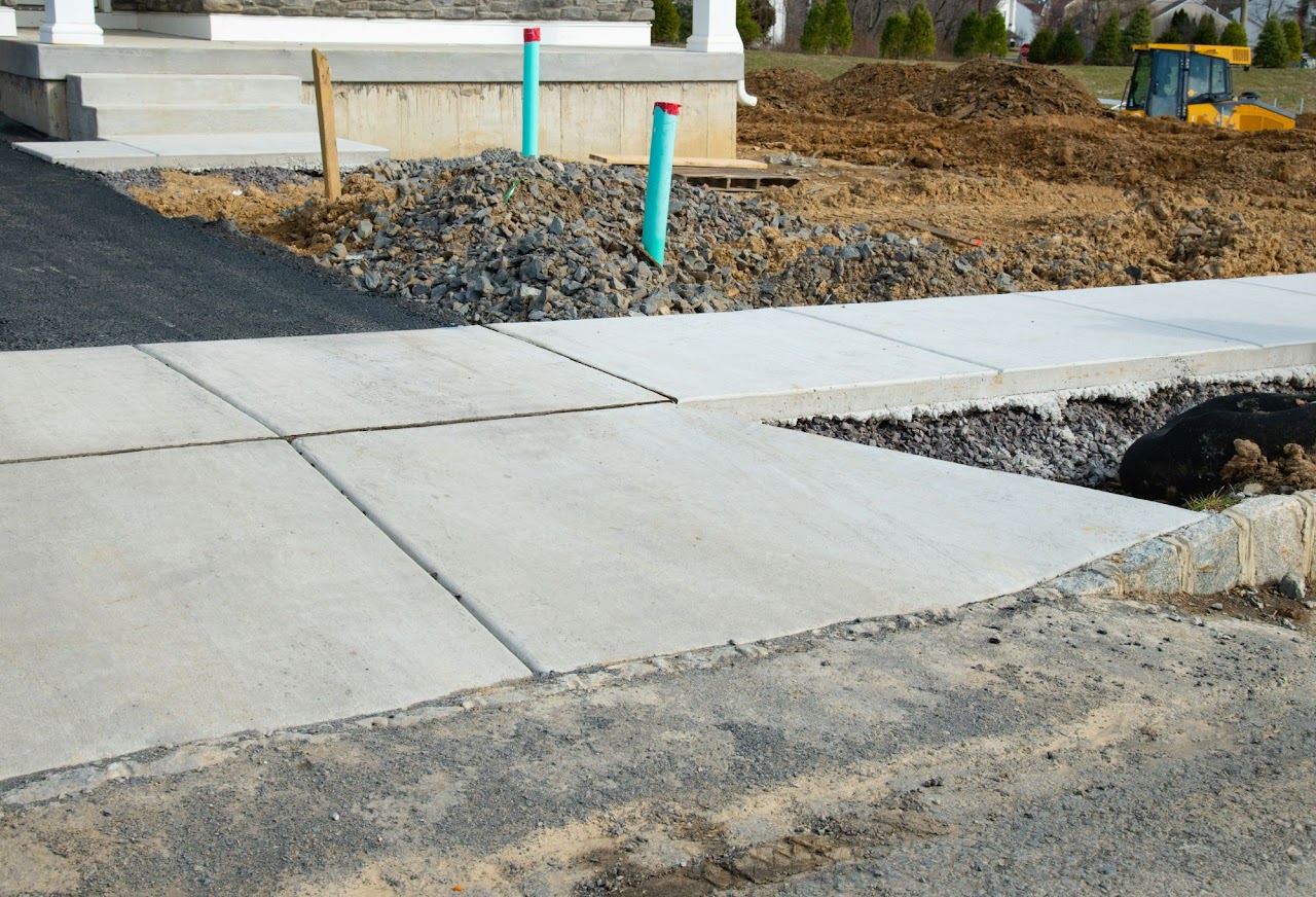 A newly constructed concrete sidewalk and curb under construction, with gravel and soil in the background, showcasing Morris Town Paving's sidewalk and curb installation and repair services in Morris County, NJ.